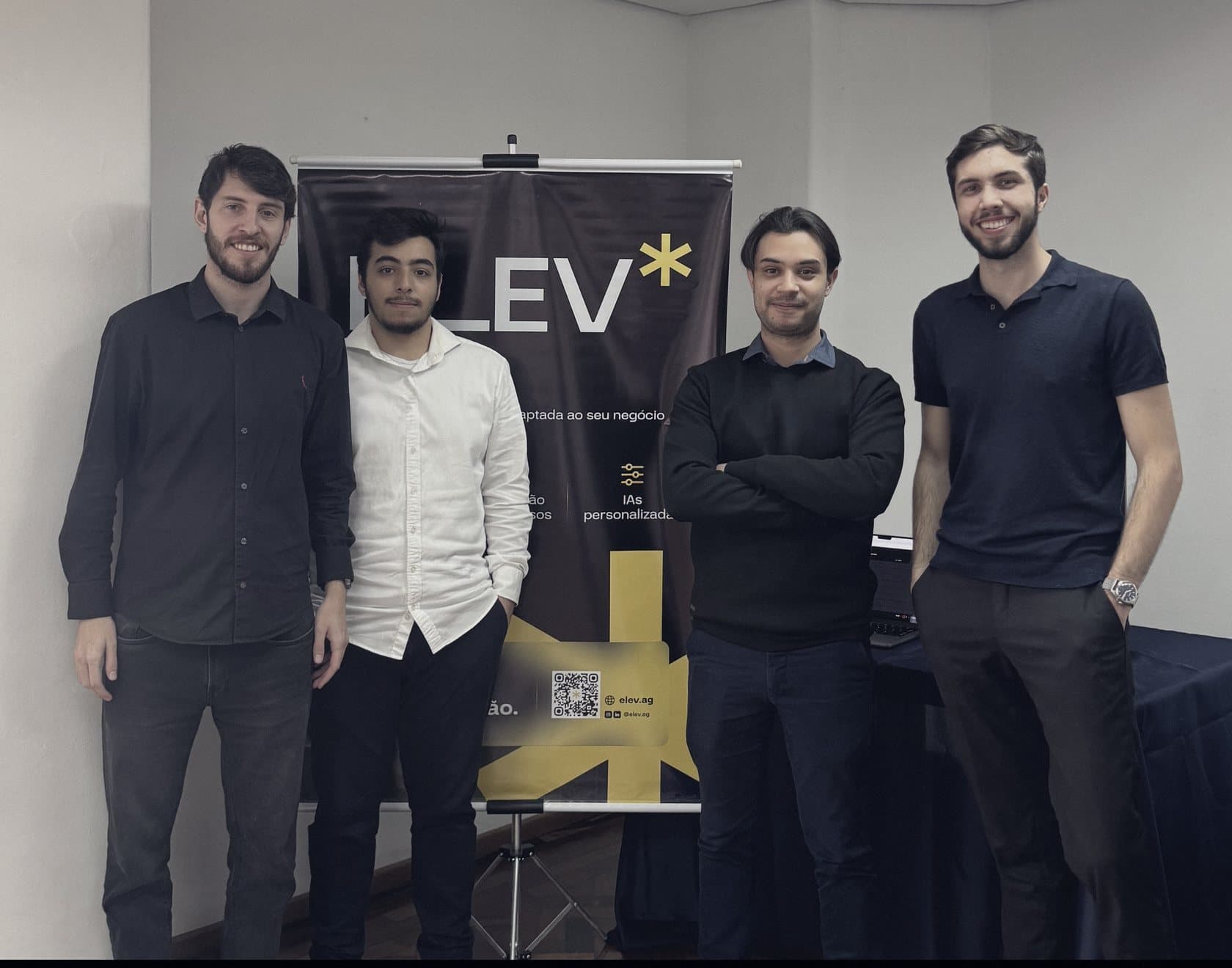 A equipe da Elev, em pé, diante do banner da empresa.